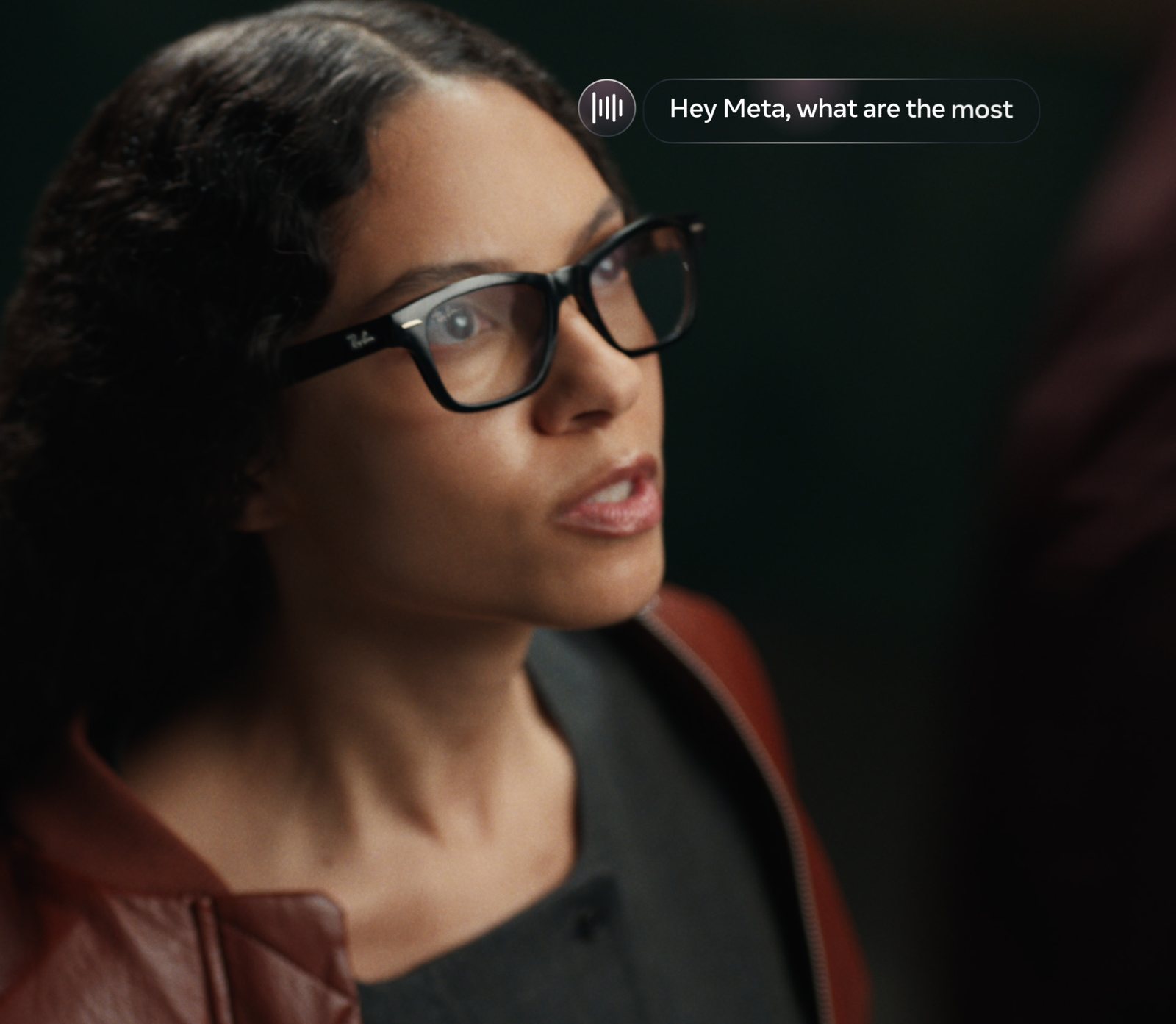 A woman wearing black rectangular Ray-Ban Meta Audio frames speaks a voice request, shown as an on-screen Hey Meta prompt