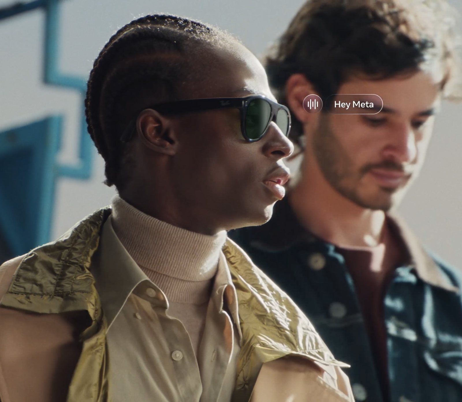 A man wearing black Ray-Ban Meta (Gen 3) sunglasses with green lenses, a Hey Meta voice prompt shown beside him
