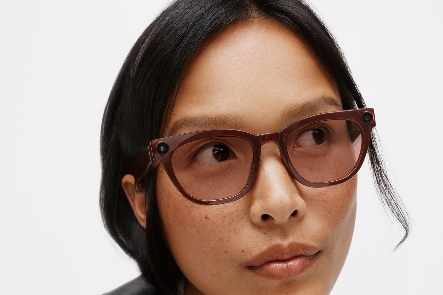 Close-up of a model wearing the brown Warby Parker frame of Samsung's Android XR glasses, with a small round lens set into each front corner